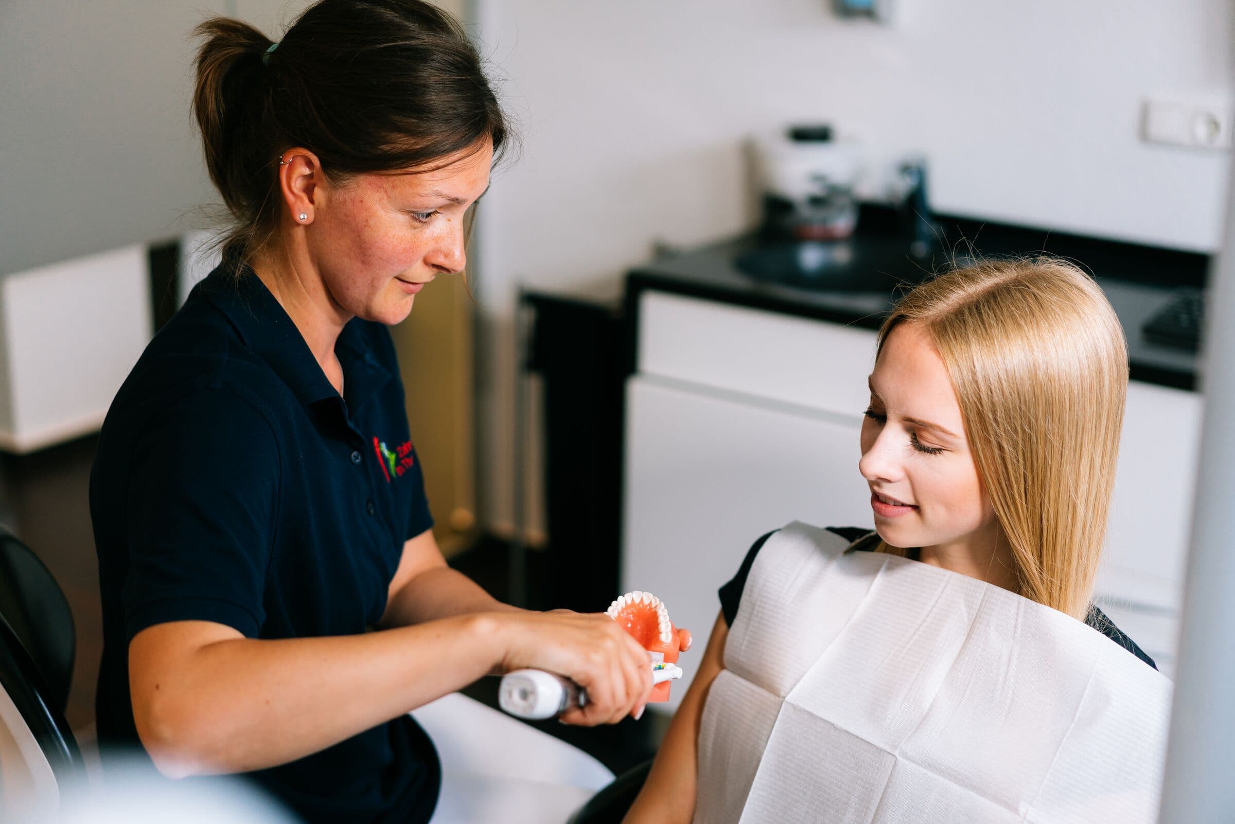 Assistentin zeigt einer Patientin die Zahnpflege am Kiefermodell